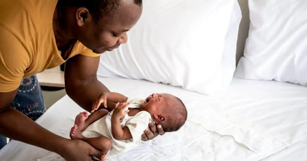 father holding crying infant next to bed